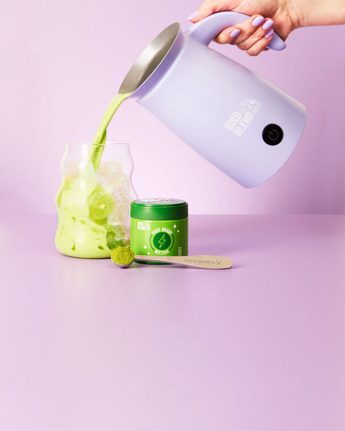 soft lilac magic whisk pouring pure grade matcha into iced matcha & pure grade tin & perfect matcha spoon filled with pure grade matcha powder