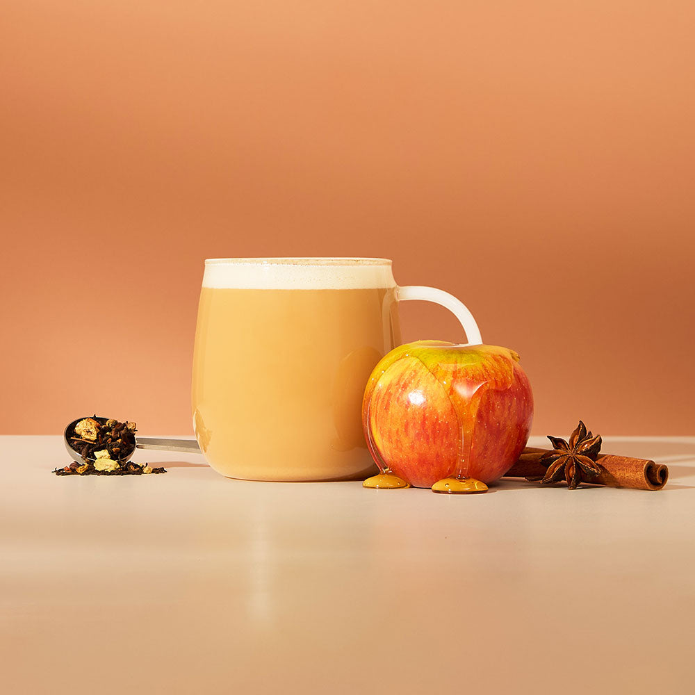 hot maple apple chai latte & ingredients including chai spices & apple covered in maple syrup and perfect tea spoon filled with loose leaf tea