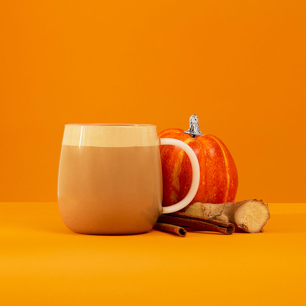 hot spiced pumpkin chai powder latte with pumpkin ginger & cinnamon stick ingredients next to glass mug
