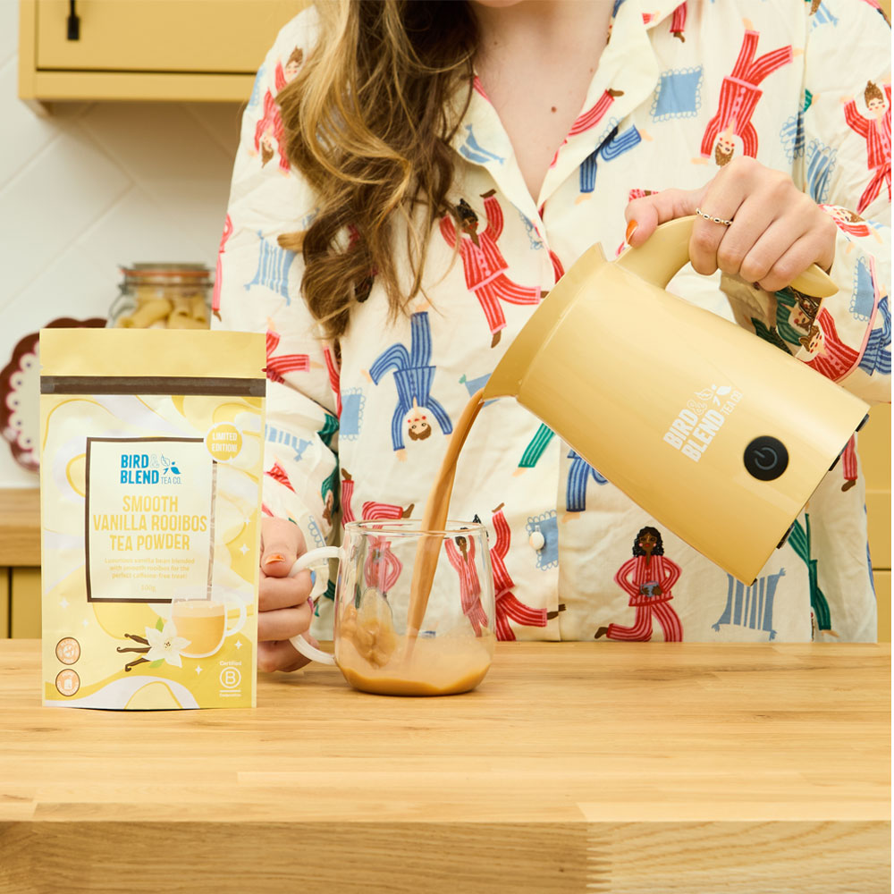 Smooth vanilla rooibos tea powder pouch & person pouring hot smooth vanilla rooibos tea powder from a bamboo gloss matcha latte magic whisk into a mug