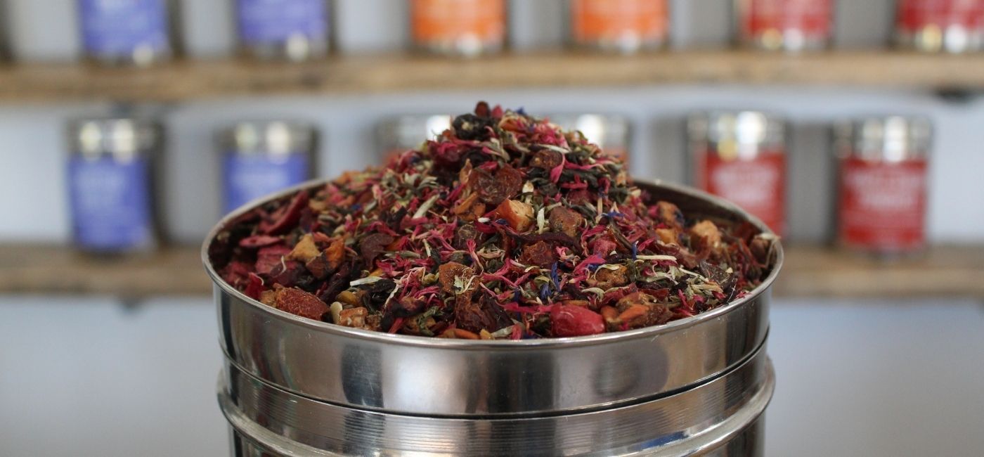 A pile of loose tea in front of shelves of tins of tea.