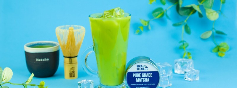 A glass of iced matcha latte and a tin of matcha tea.