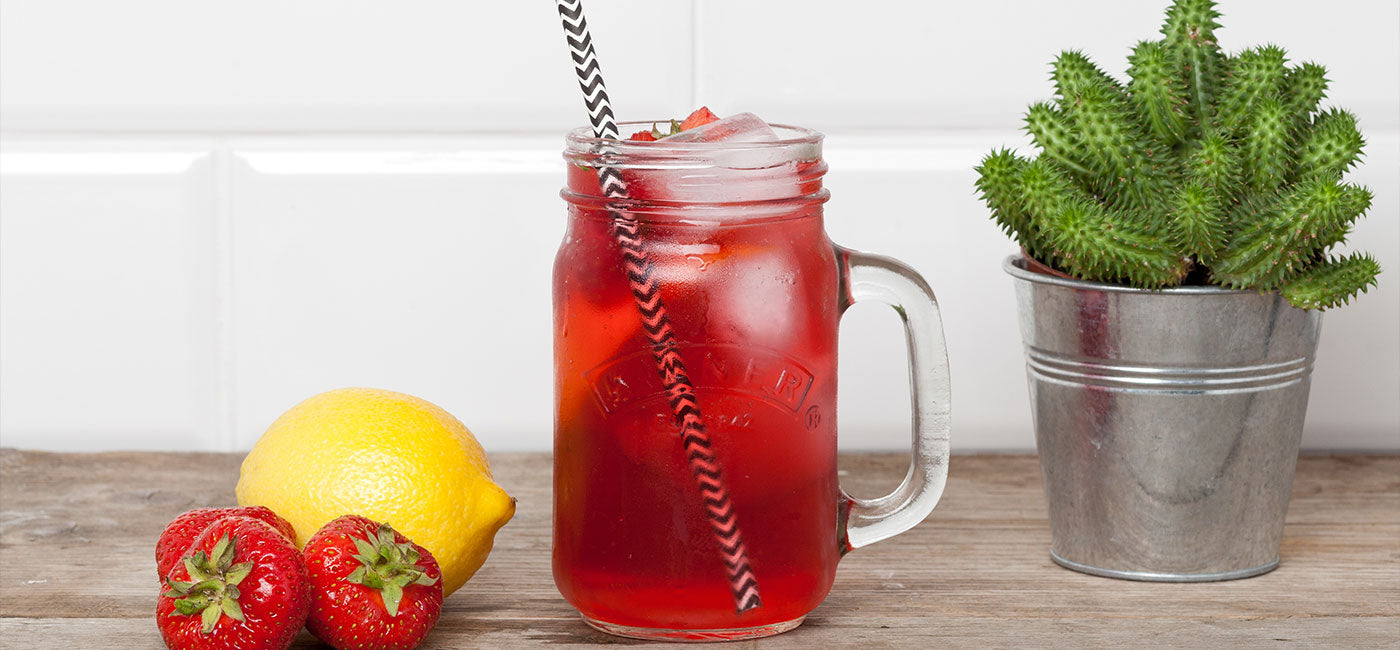 glass of Strawberry Lemonade iced tea cocktail, next to two strawberries and a lemon