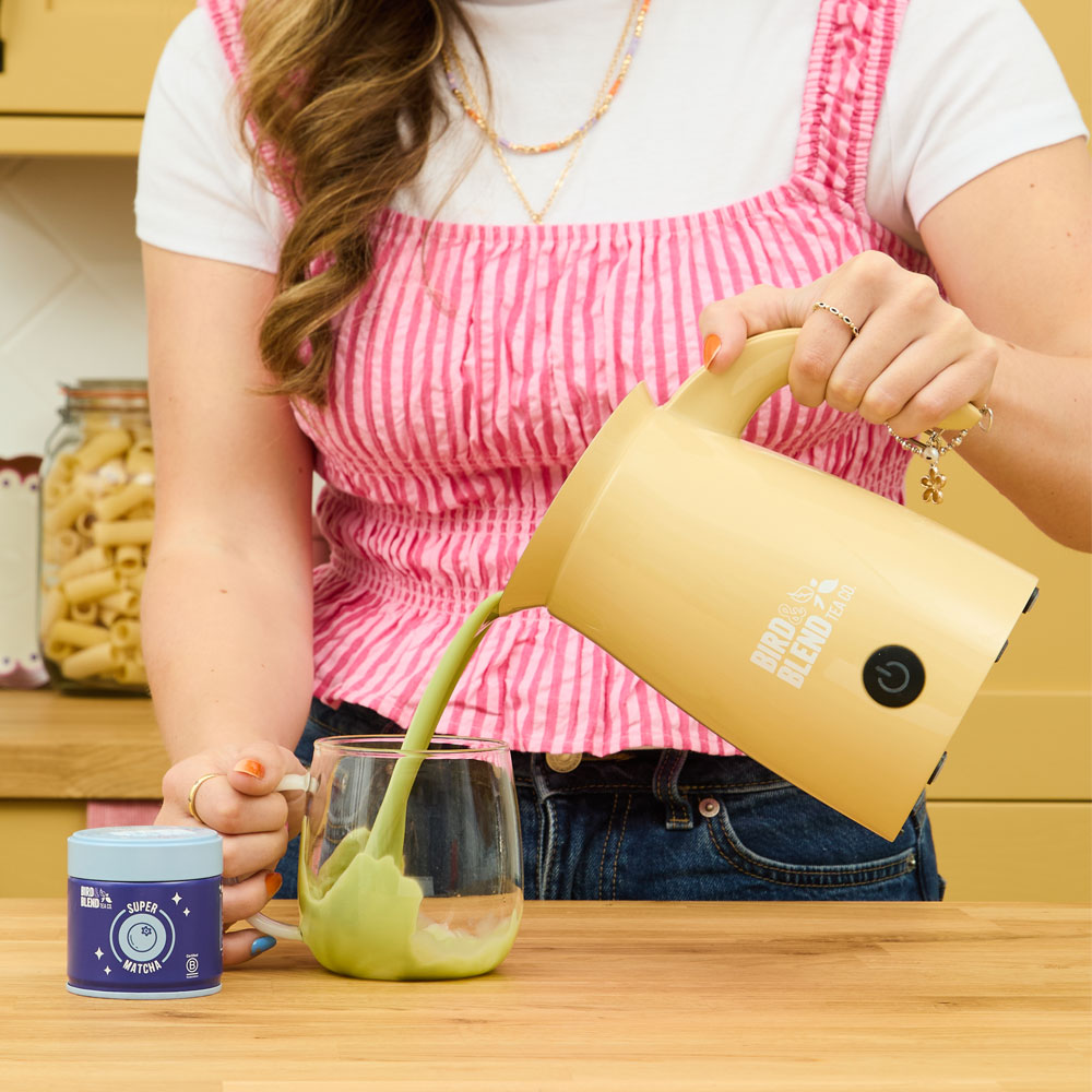 blueberry & acai super matcha tin and person pouring hot blueberry & acai super matcha from a bamboo gloss matcha latte magic whisk