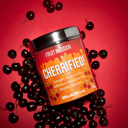 cherrified! hero tea tin laying in a bed pf cherrys on a red background