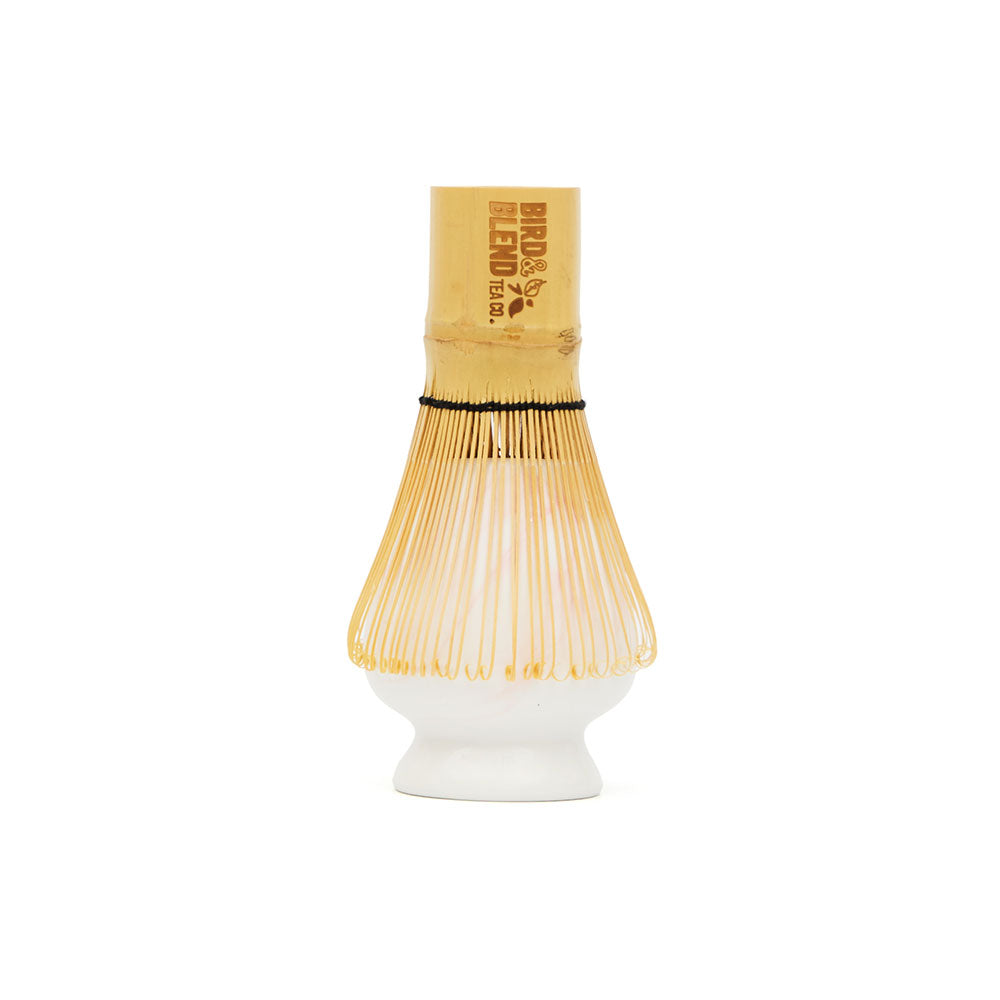 traditional bamboo matcha tea whisk on top of white and pink marbled matcha tea whisk holder